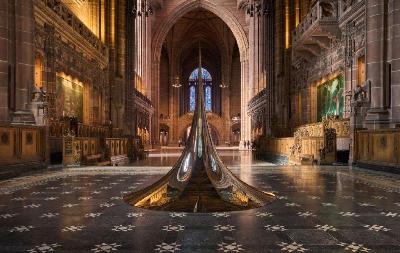 An art structure of a circular peak sits on the chequered floor of a cathedral.