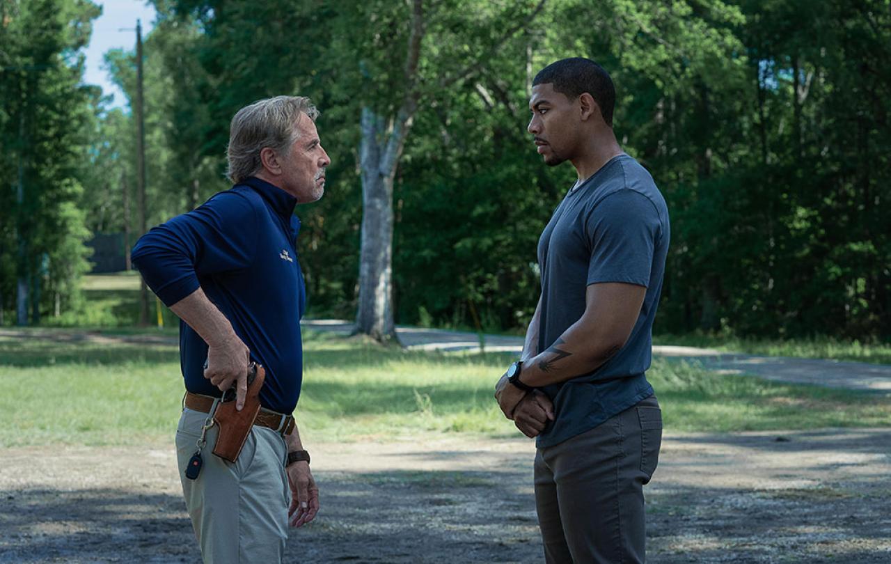 Two men stand off against each other, one holds a holstered gun.