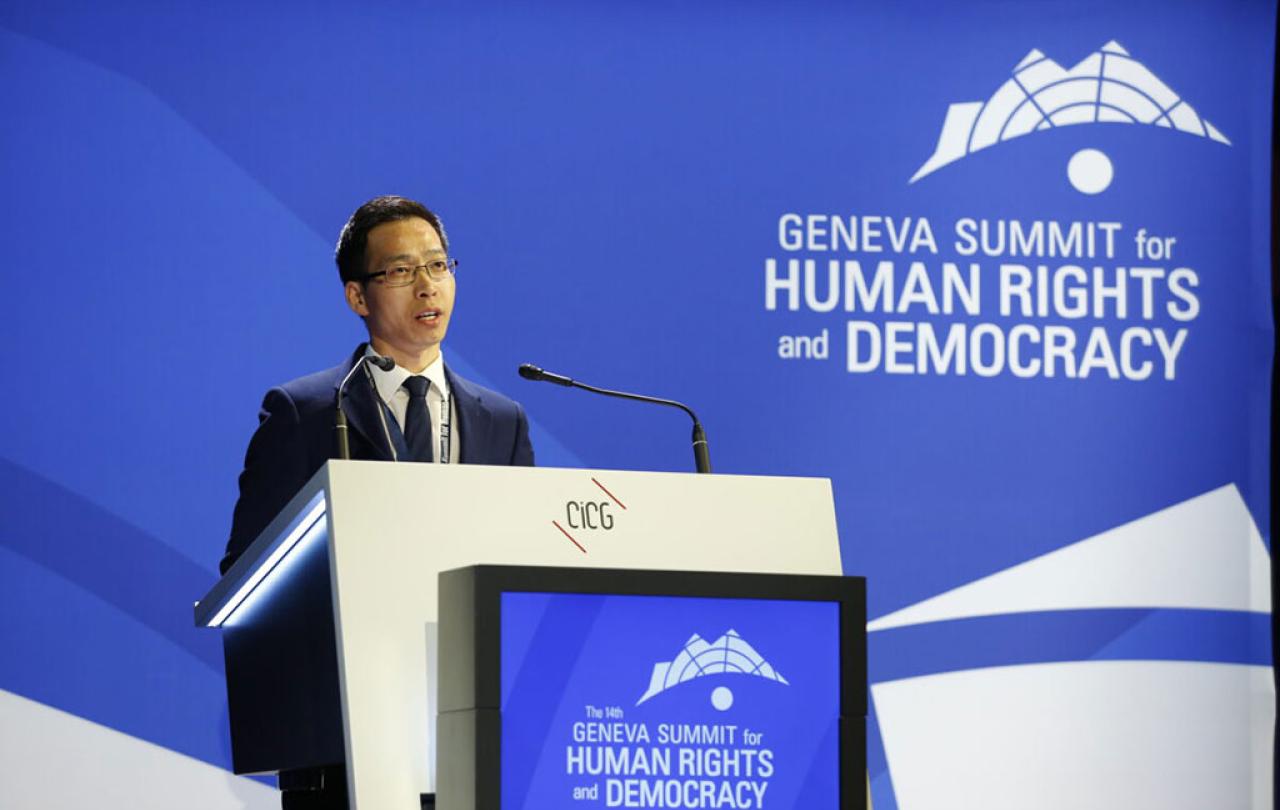 A conference speaker at a podium against a backdrop of blue.