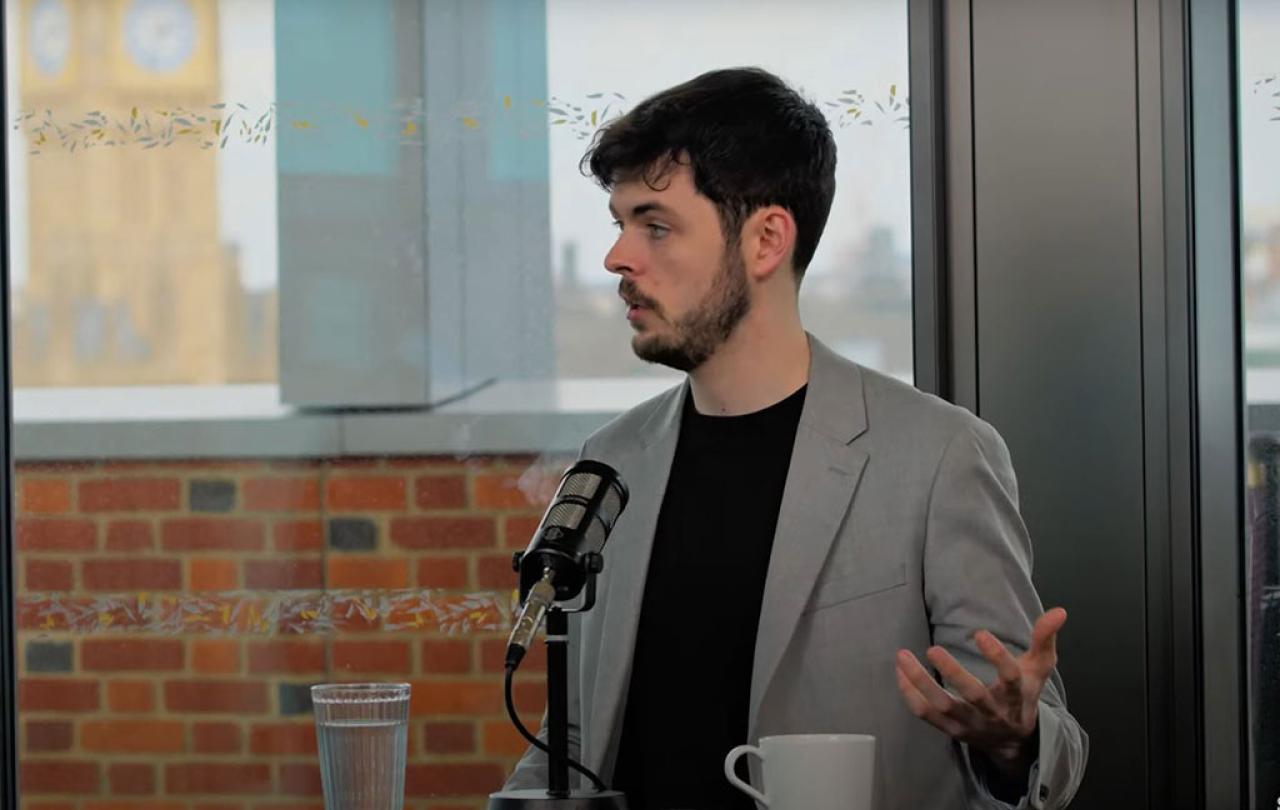 A podcast guest speaks in front of a mic and raises their hand to gesture.