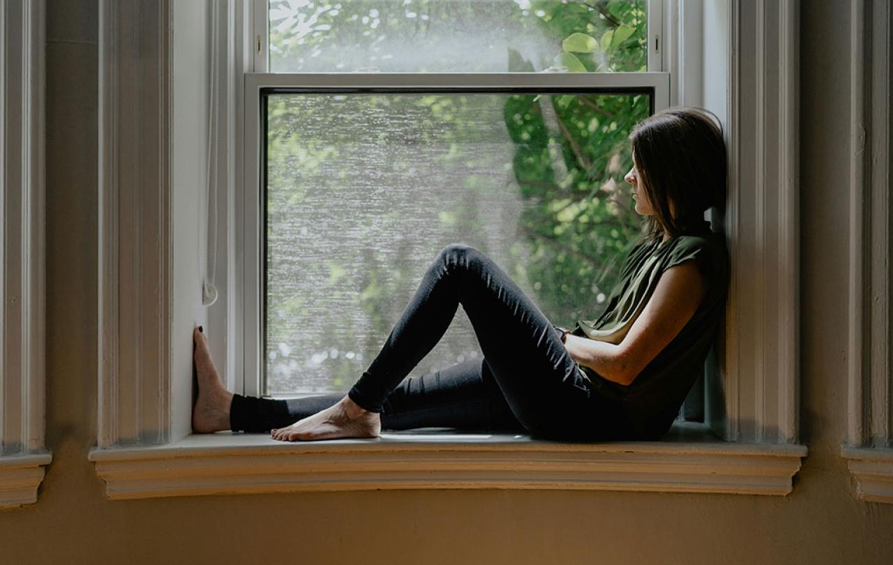 A person sits on a window sill with one raise knee.