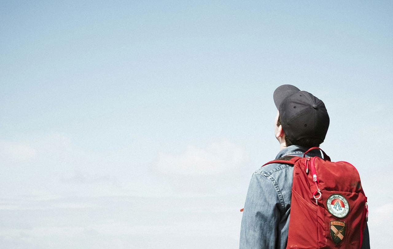 A person wearing a backpack looks to the sky.