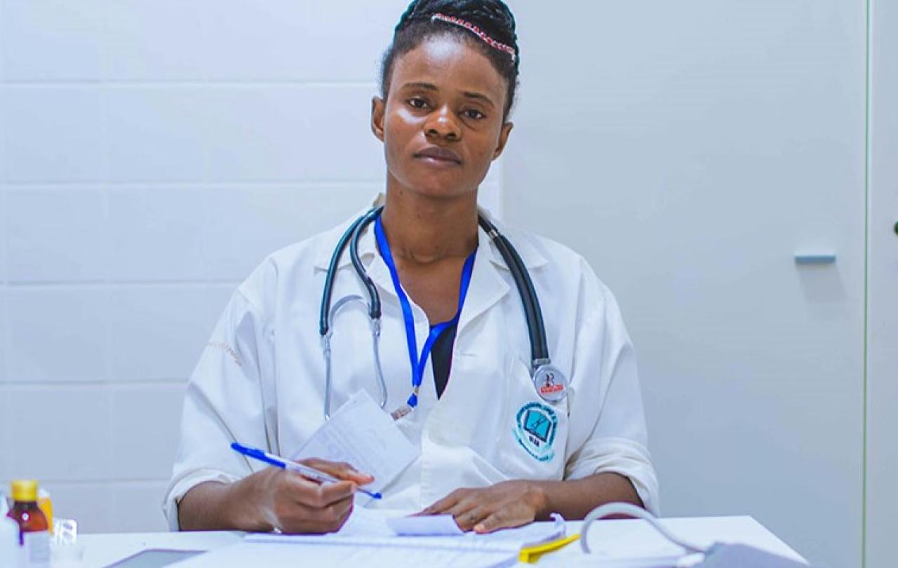 A tired-looking doctor sits at a desk dealing with paperwork.