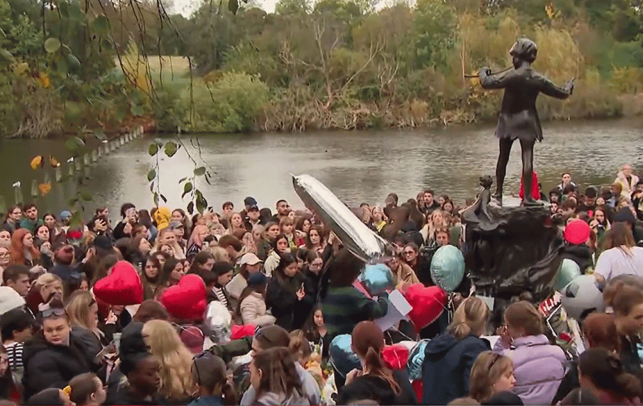 A crowd of teenagers gather by a Peter Pan statue to mourn a dead pop star