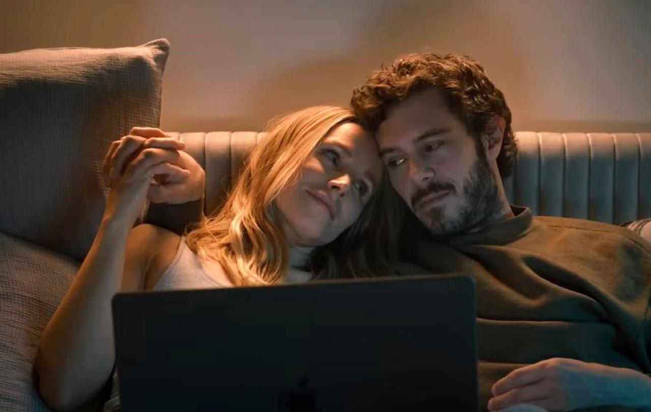 A couple together on a sofa watch a laptop,