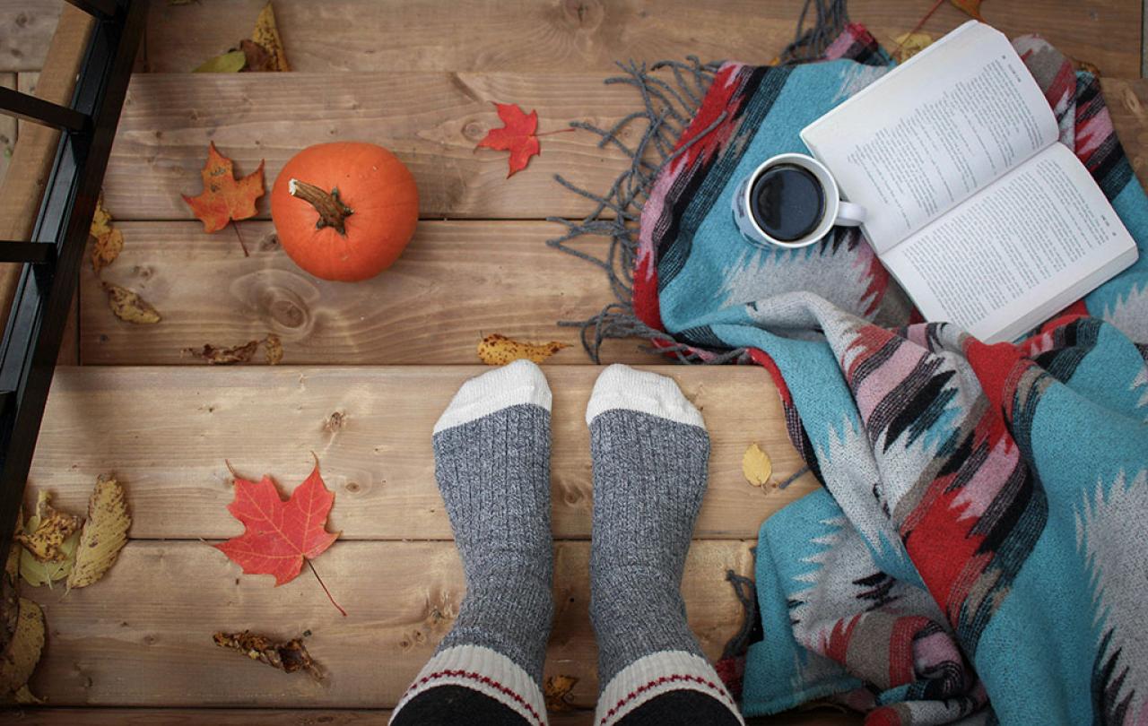 A set of be-socked feat rest on a leaf strewn step beside a book and a cup of coffee.