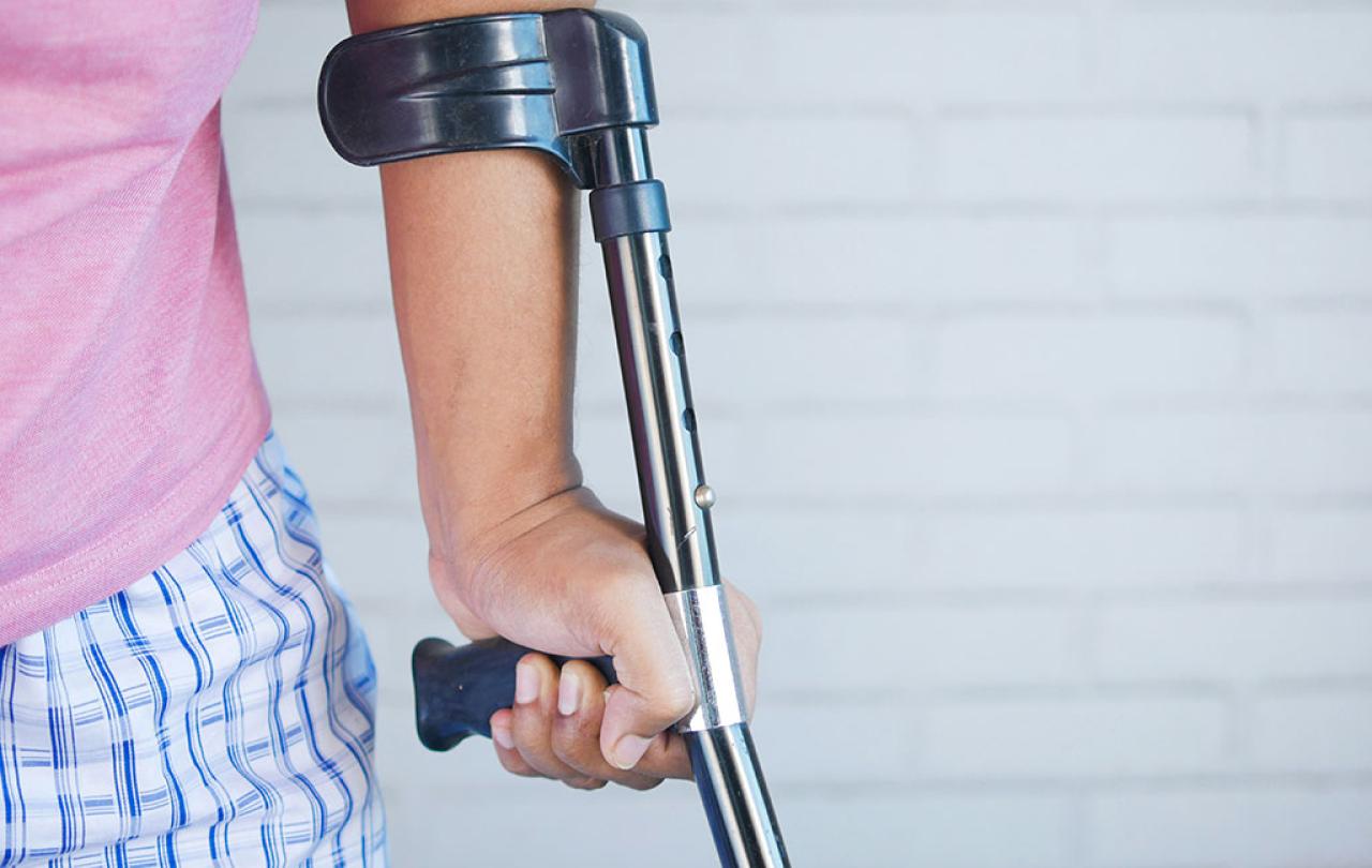 A crutch is held in the hand of someone in pyjamas.