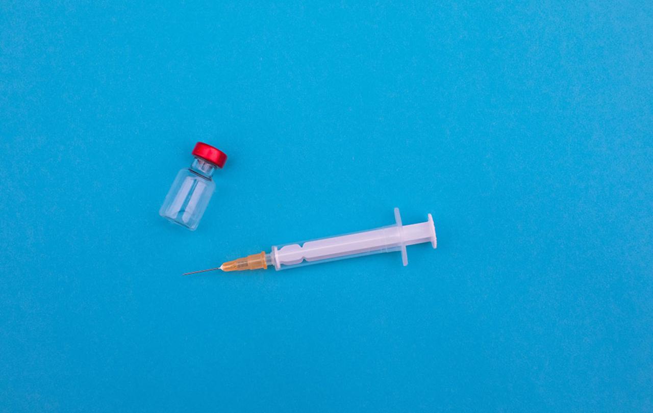 A vial and syringe lie on a blue backdrop.