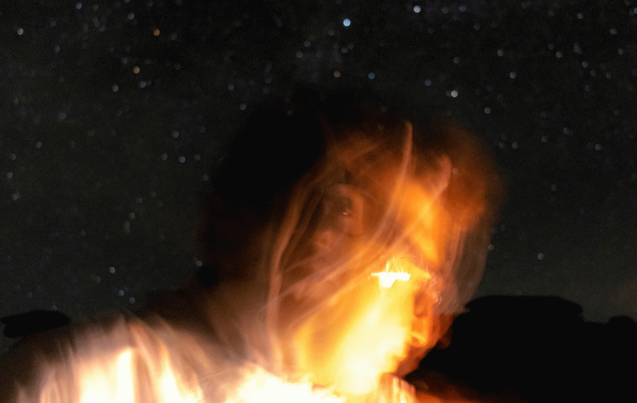 Against a night sky a lit up face is blurred by the camera movement.