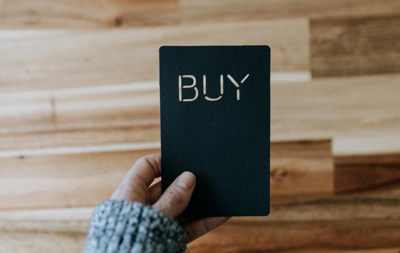 a hand hold a black payment card that reads 'buy'.