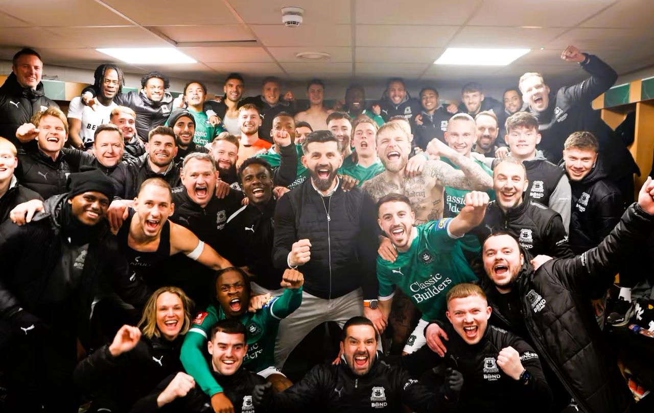 in a dressing room, celebrating footballer crowd together for a photograph.