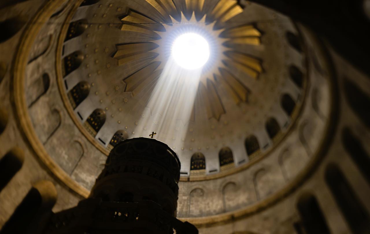 A shaft of light from an opening in a dome lights a cross on a pedestal.