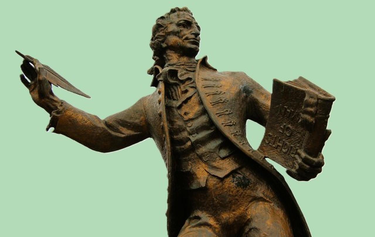 A statue of a 18th century man holding a pen and a book.