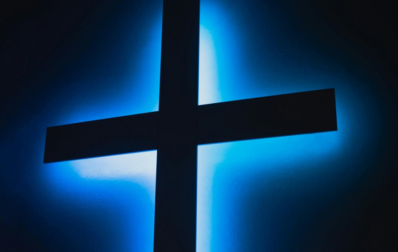 A black cross is backlit bya blue light.