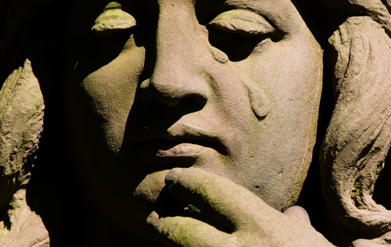 A stone statue's face depicts a falling tear.