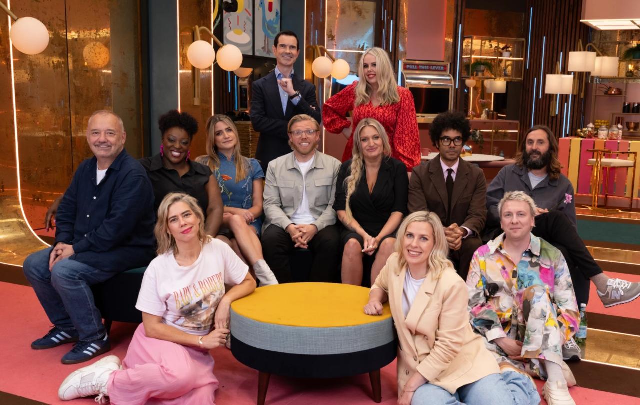 A group of comedians pose on a TV show set.