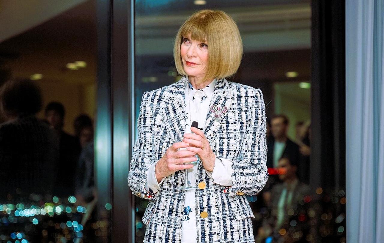 Anna  Wintour stands holding a small mic.