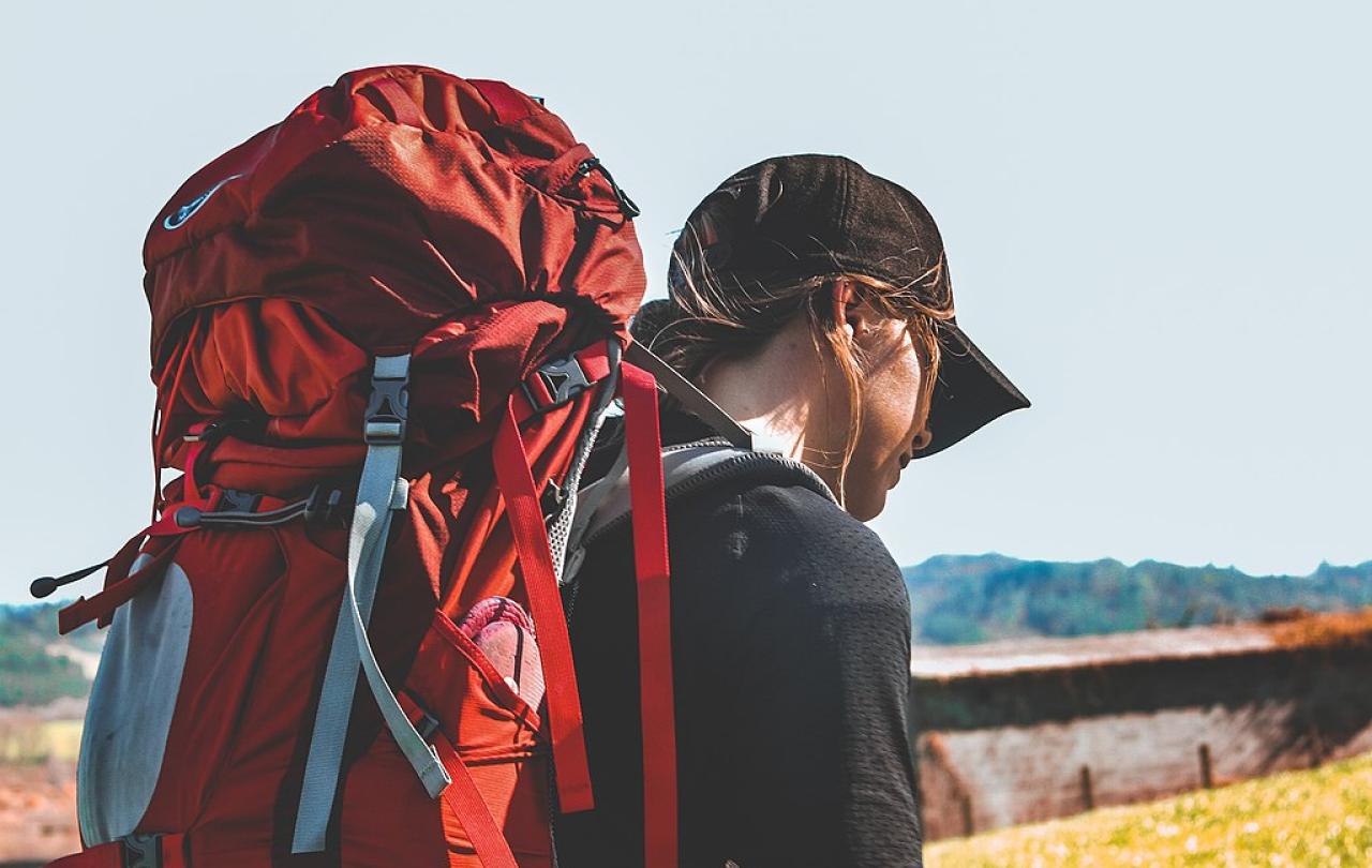 A pilgrim with a red backpack heads off.