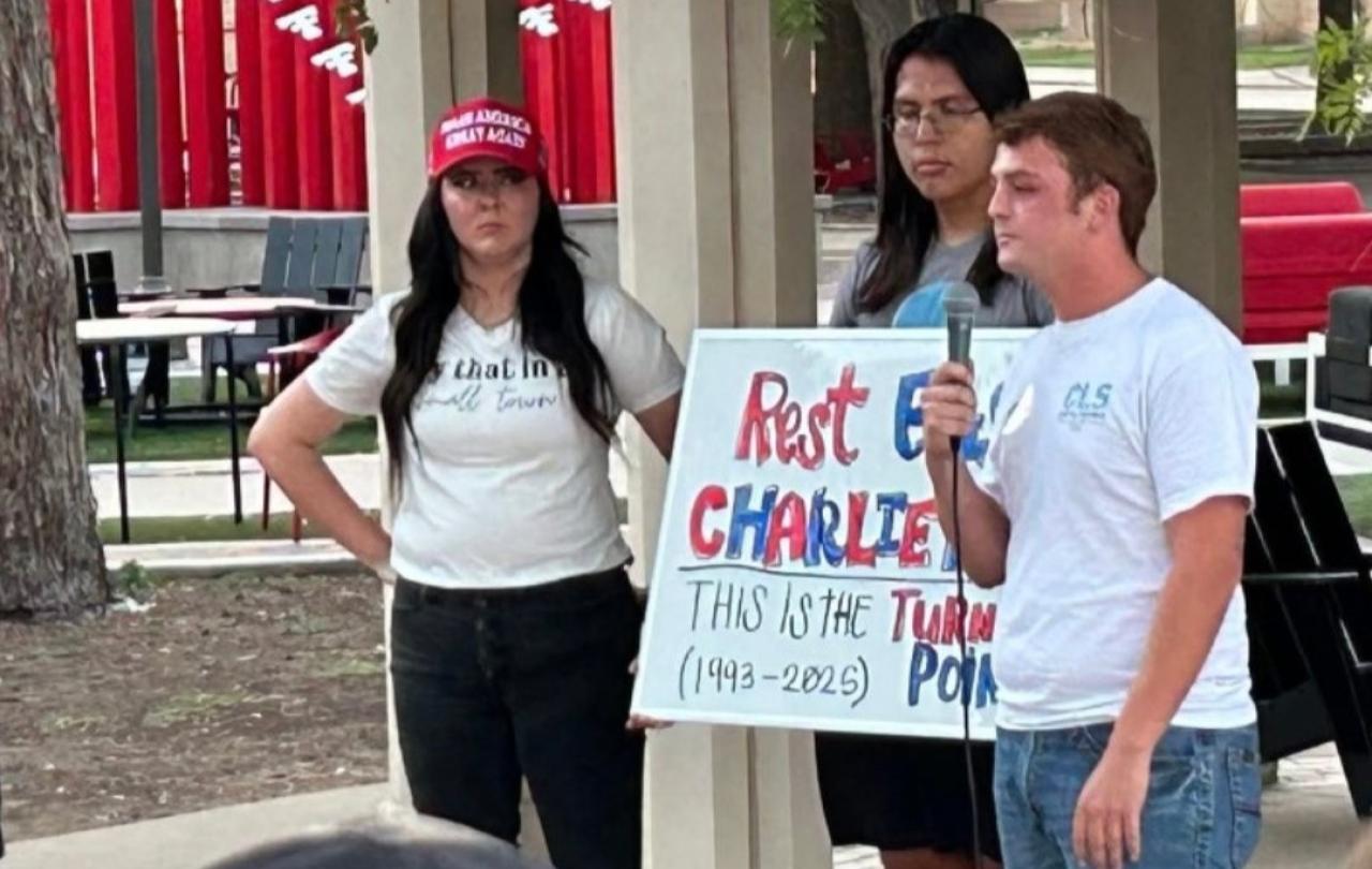 Mourning students at a vigil hold a sign about Charlie Kirk.