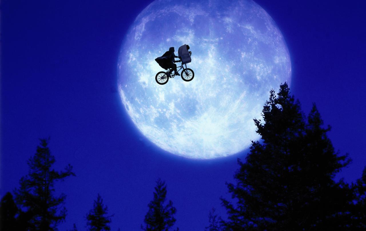 A child and E.T. ride a BMX bike across a moon lit sky.