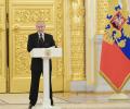 Preisdent Putin stands behind a lectern with a gold door and Russian flag behind him.