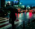 On a rainy night a pedestrian, holding a brolly, waits to cross a road.