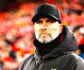 A stern looking  football manager stares hard, with a stand of supporters behind him.