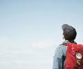 A person wearing a backpack looks to the sky.