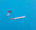 A vial and syringe lie on a blue backdrop.