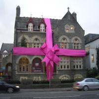 A large stone house is wrapped in a red ribbon and bow.