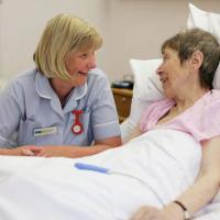 A nurse bends beside a bed and talks to a patient