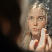 A woman sees her reflection in a mirror and hold a finger up.