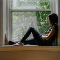 A person sits on a window sill with one raise knee.