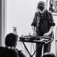 A woman stand at a mixing desk playing a small keyboard.