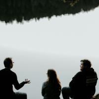 Three people sitting looking out over viewpoint are silhouetted against the sky. 